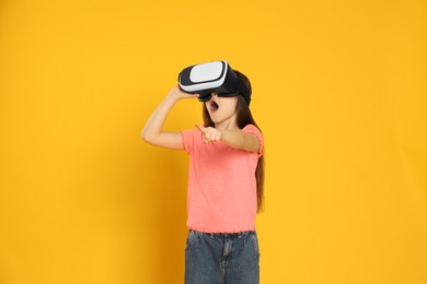 Emotional little girl using virtual reality headset on yellow background