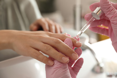 Photo of Professional manicurist pouring oil on client's nails in beauty salon, closeup