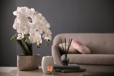 Photo of Beautiful orchid, burning candles and air reed freshener on table indoors