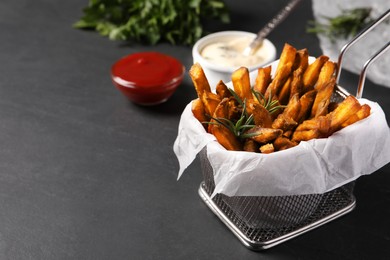 Frying basket with sweet potato fries and sauces on black table. Space for text