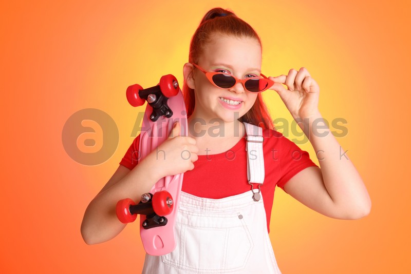 Cute indie girl with sunglasses and penny board on color background