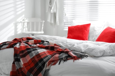 Comfortable bed with warm checkered plaid in stylish room interior