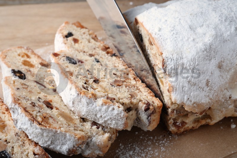 Cutting traditional Christmas Stollen with knife on parchment paper, closeup