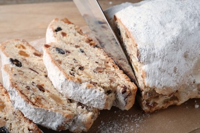 Cutting traditional Christmas Stollen with knife on parchment paper, closeup