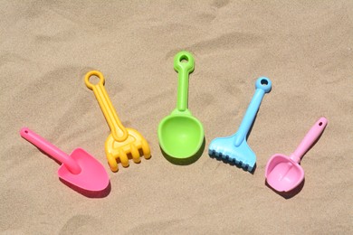 Photo of Bright plastic rakes and shovels on sand, above view. Beach toys