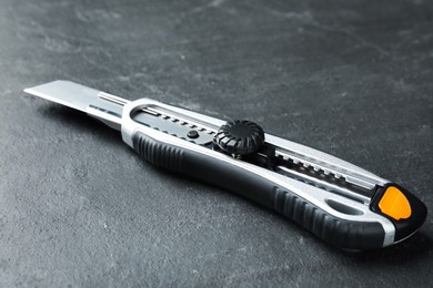 Utility knife on black table, closeup. Construction tool