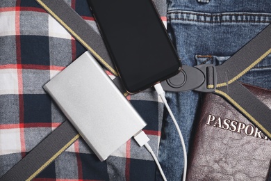 Smartphone charging with power bank, passport and clothes in open suitcase, top view
