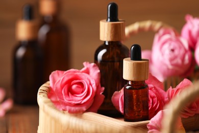 Tray with bottles of essential rose oil and flowers on table, closeup