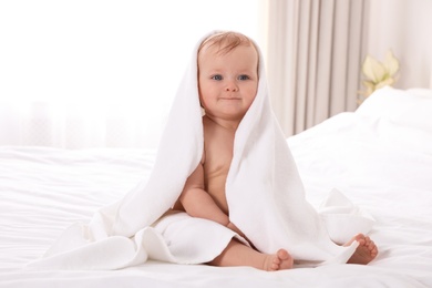 Cute little baby with soft towel on bed after bath