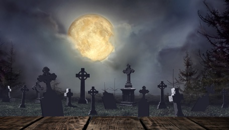 Wooden surface and moonlit graveyard with old creepy headstones on Halloween