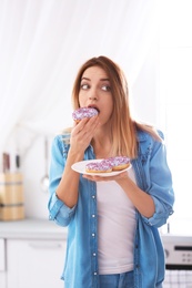 Photo of Emotional young woman eating donut in kitchen. Failed diet
