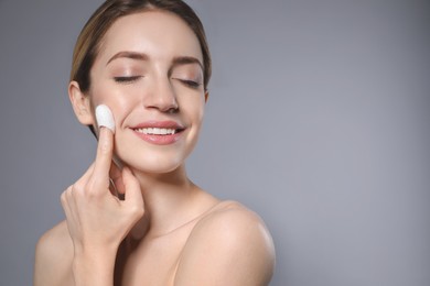 Woman using silkworm cocoon in skin care routine on grey background. Space for text