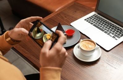 Male blogger taking photo of dessert and coffee at table in cafe, closeup