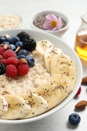 Tasty oatmeal porridge with berries, banana and chia seeds on light table, closeup