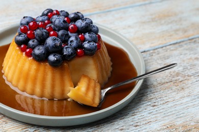 Photo of Delicious pudding with caramel, blueberries and redcurrants on wooden table