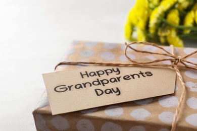 Gift box and tag with phrase Happy Grandparents Day on light background, closeup