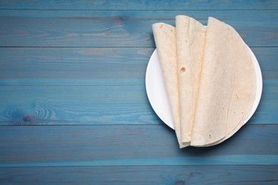 Photo of Delicious folded Armenian lavash on light blue wooden table, top view. Space for text