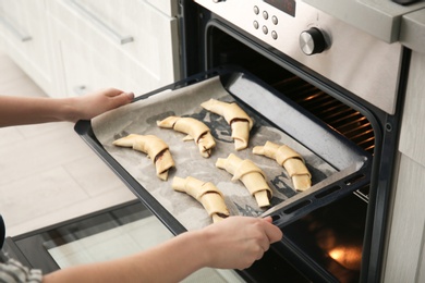 Woman putting baking sheet with raw croissants in oven, closeup