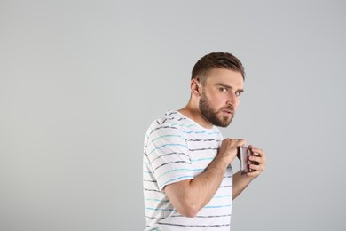 Greedy young man hiding wallet with money on light grey background, space for text