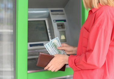 Woman with money near cash machine outdoors, closeup