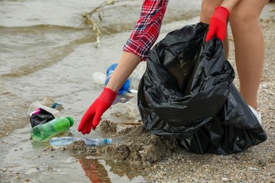 Photo of Woman in gloves with trash bag collecting garbage on beach, closeup
