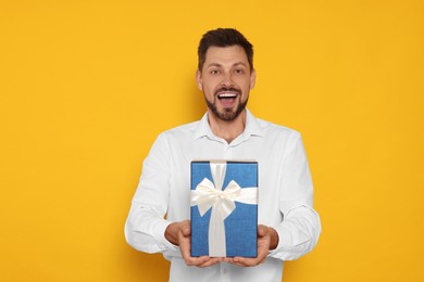 Photo of Happy man with gift box on yellow background