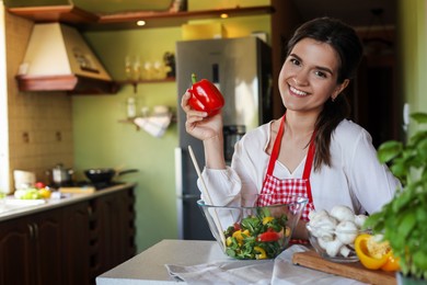 Young woman with fresh bell pepper and bowl of salad at countertop in kitchen, space for text