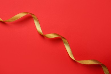 Beautiful golden ribbon on red background, top view