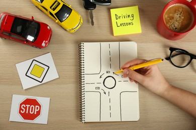 Woman with workbook for driving lessons and road signs at wooden table, top view. Passing license exam