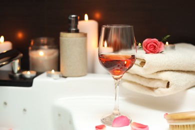 Wine in glass, towels and rose on edge of bath indoors. Romantic atmosphere
