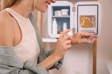 Woman taking cosmetic product from mini fridge indoors, closeup