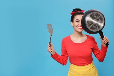 Photo of Housewife with frying pan and spatula on light blue background, space for text