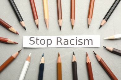 Phrase Stop Racism and colorful pencils on light grey table, flat lay