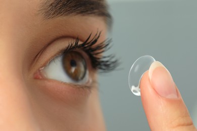 Woman putting contact lens in her eye on grey background, closeup