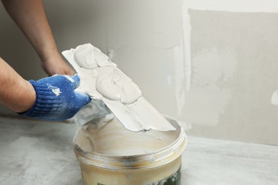 Professional worker holding putty knife with plaster indoors, closeup. Space for text