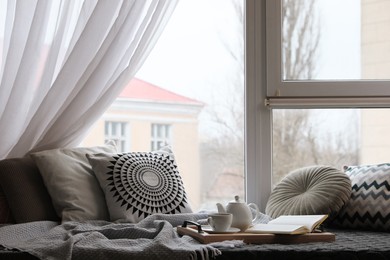 Comfortable lounge area with blanket and soft pillows near window in room