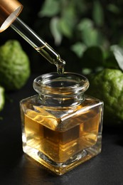 Dripping bergamot essential oil into glass bottle on black stone table