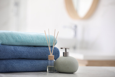 Stack of fresh towels, reed air freshener and soap dispenser on table in bathroom