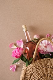 Wicker bag with bottle of rose wine and beautiful pink peonies on brown background, top view. Space for text