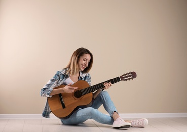 Young woman playing acoustic guitar near grey wall