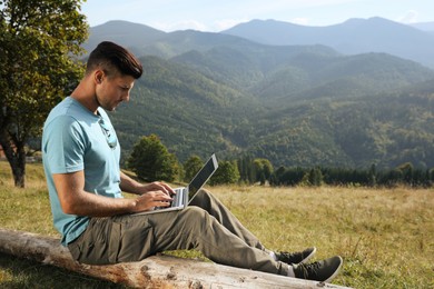 Man working with laptop in mountains on sunny day