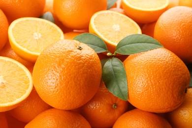 Cut and whole fresh ripe oranges with green leaves as background, closeup