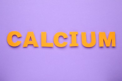 Word Calcium made of orange paper letters on violet background, top view