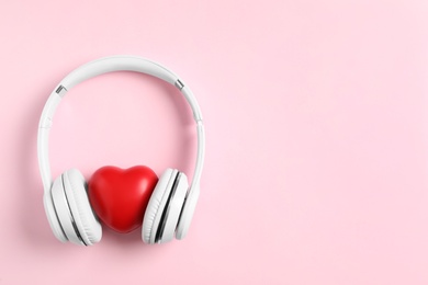 Modern headphones and red heart on pink background, flat lay with space for text. Listening love music songs