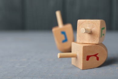 Hanukkah traditional dreidels with letters Gimel and He on grey wooden table, closeup. Space for text