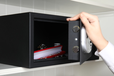 Woman opening black steel safe with money and jewelry on shelf, closeup
