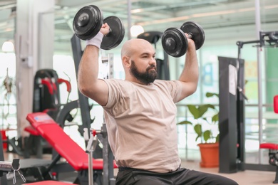 Overweight man training with dumbbells in gym