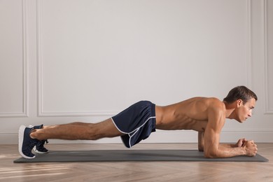 Handsome man doing plank exercise on floor indoors