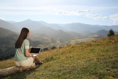 Young woman working with laptop in mountains on sunny day