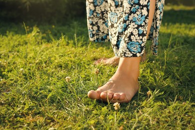 Woman walking barefoot on green grass, closeup. Space for text